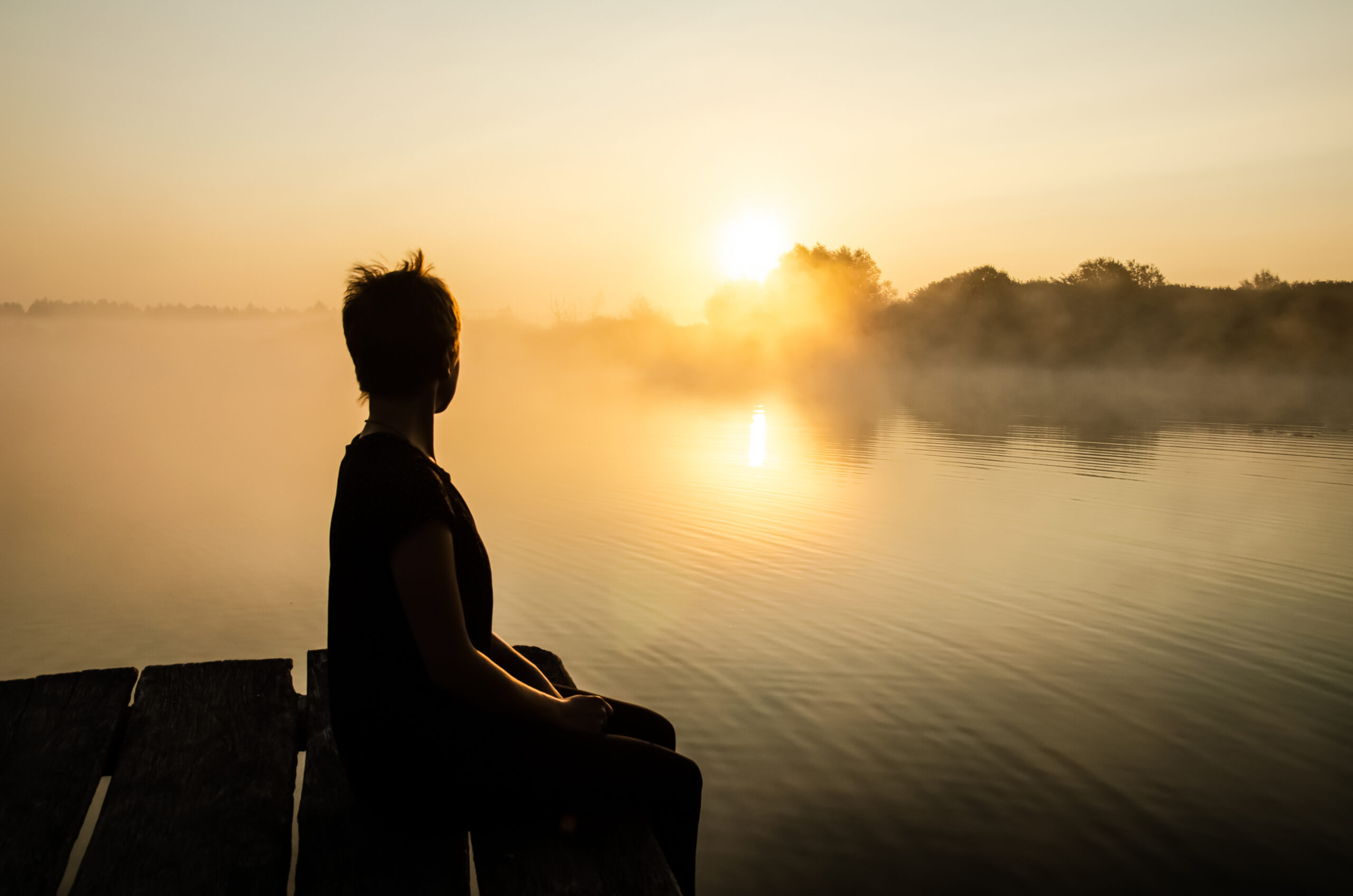 Frau sitzt an einem See und betrachtet den Sonnenuntergang. Ikigai - lebe deine wahre Essenz